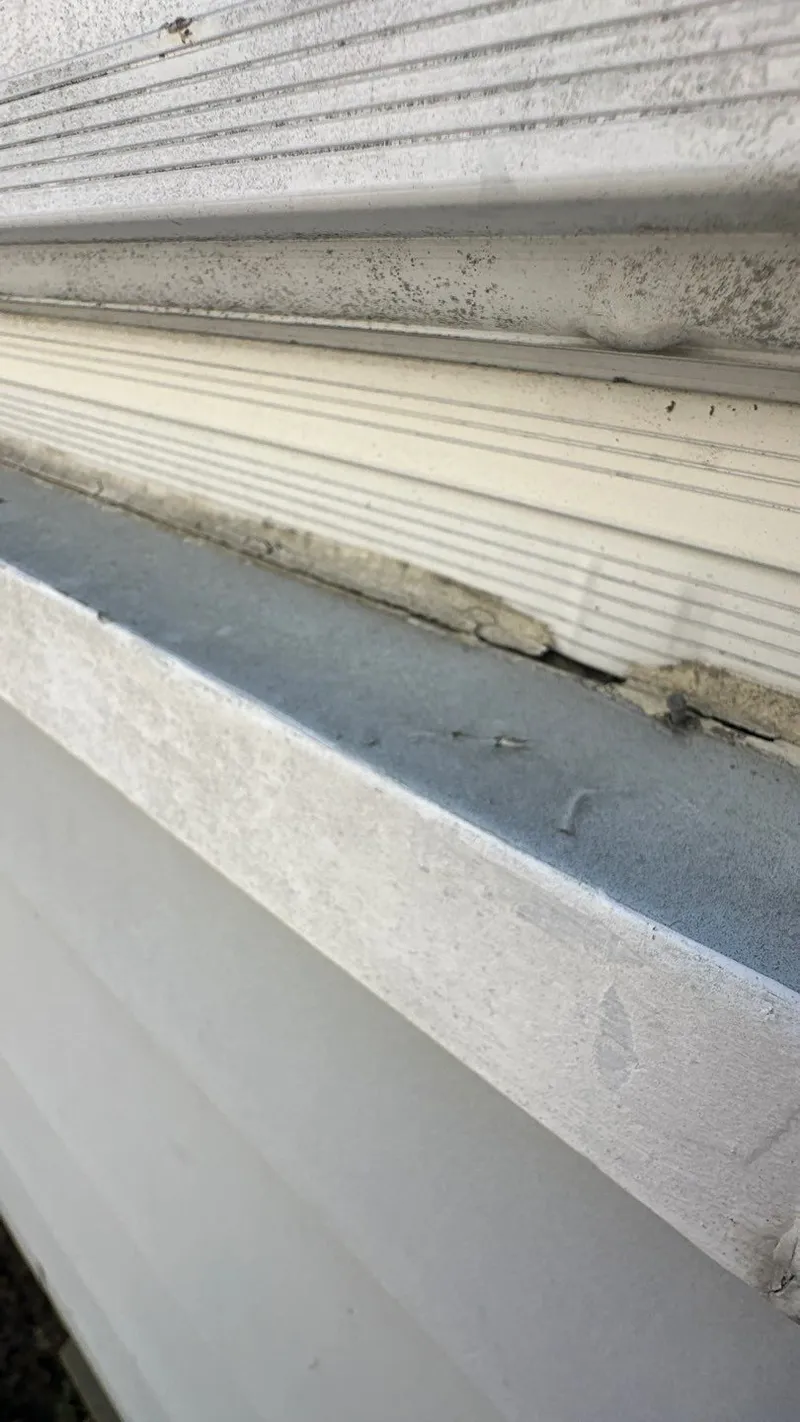 Dented soft metal at a window sill — hail damage is rarely limited to the roof.
