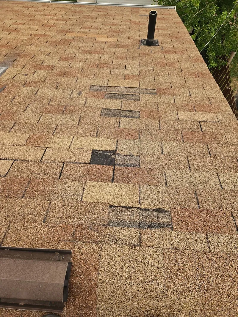 Missing shingles expose the roof deck — field-marked storm damage, not age.