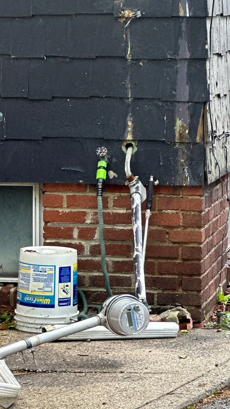 The tear-out point: damaged shingle siding where the mast ripped away, with the meter and conduit on the ground below.